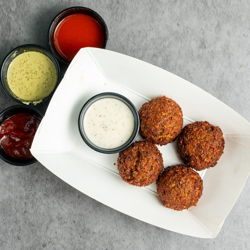 Crispy falafel balls in a white tray served with creamy herb sauce and three dipping sauces.