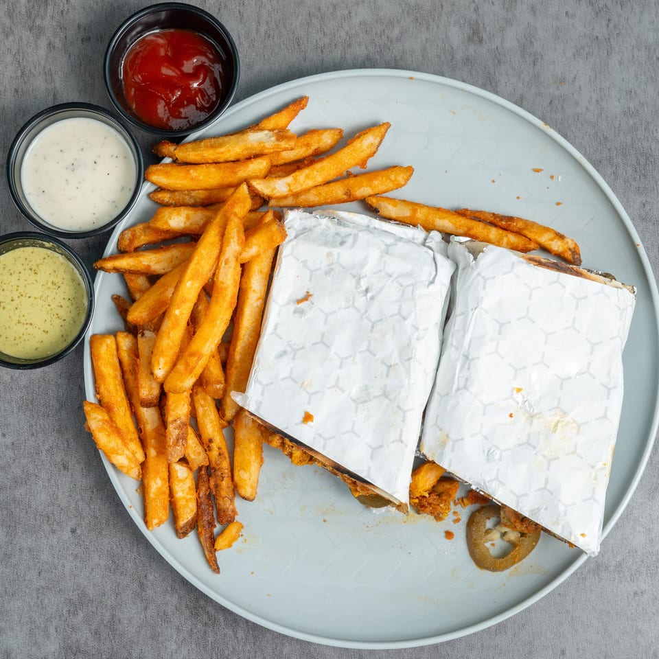 Overhead view of wrapped sandwiches with crispy fries and three dipping sauces on a large plate.