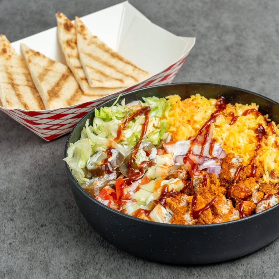 Loaded bowl of seasoned rice, crispy chicken, lettuce, vegetables, and drizzled sauces served with grilled pita triangles.