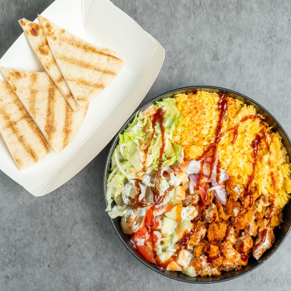 Overhead view of grilled folded flatbreads beside a bowl of yellow rice, crispy chicken, lettuce, vegetables, and drizzled sauces.